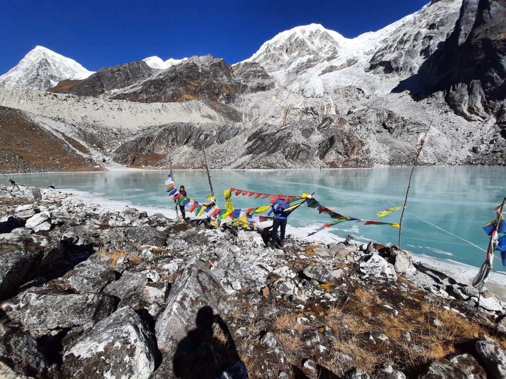 People pray at the side of a mountain lake, with colourful flags