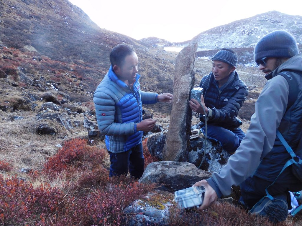 Three people attach a camera trap to a rock