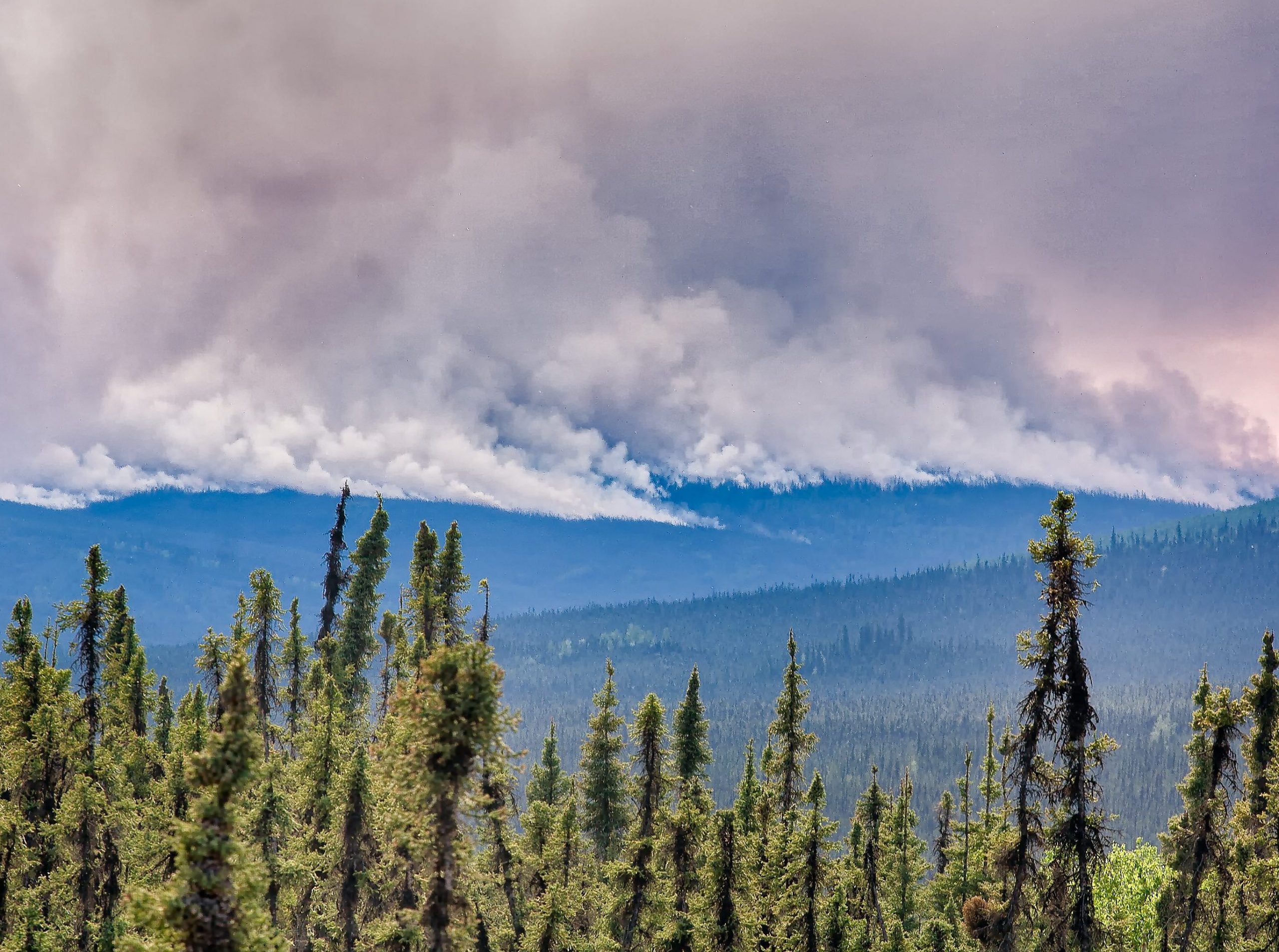 A scenic Alaskan wilderness with wildfires burning on the horizon