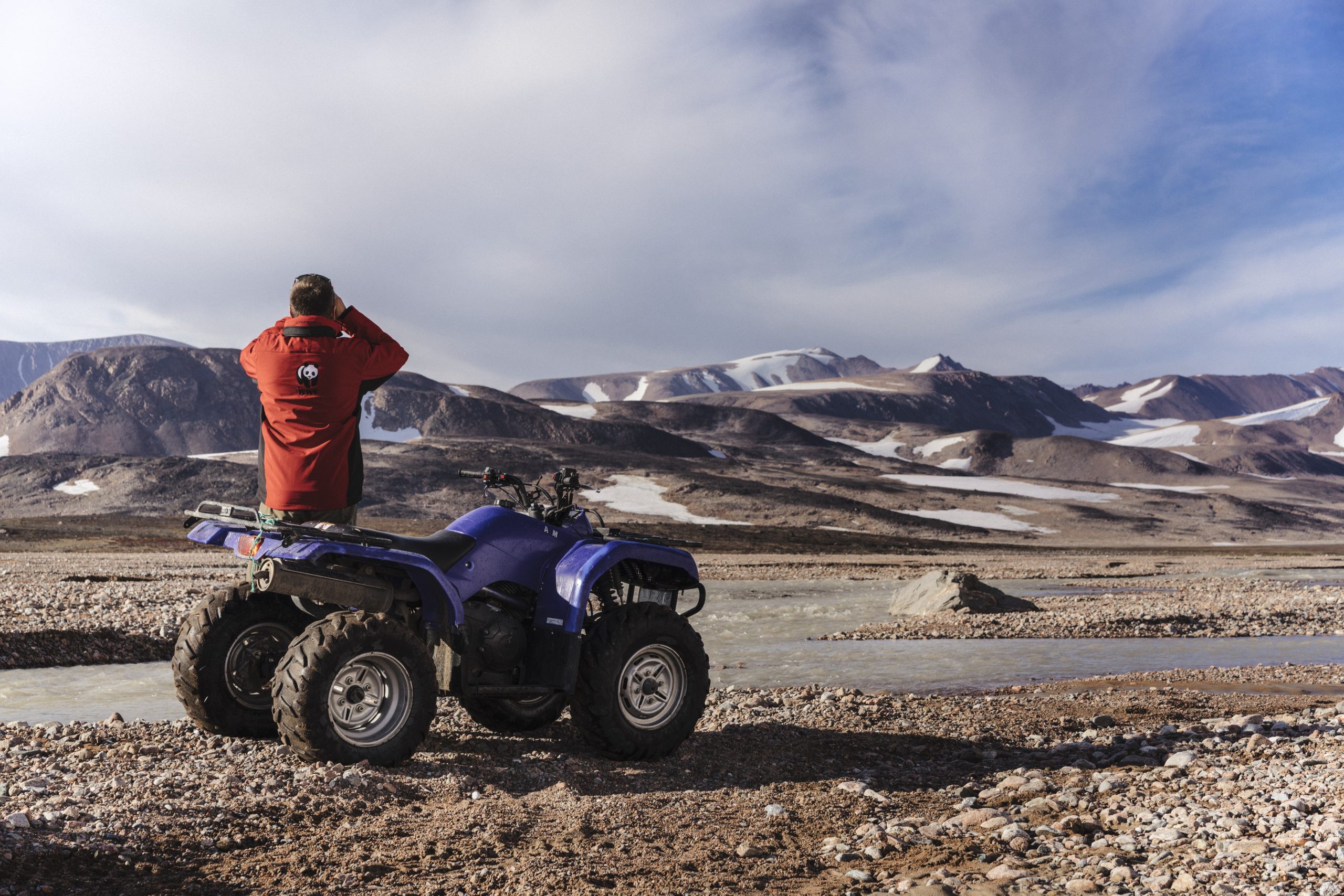 A member of Greenland's polar bear patrol surveys the landscape next to a quad bike