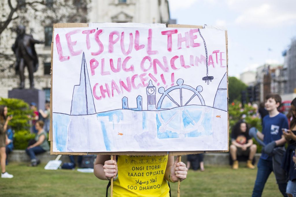 Child posing behind handheld placard which reads: “Let’s pull the plug on climate change.”