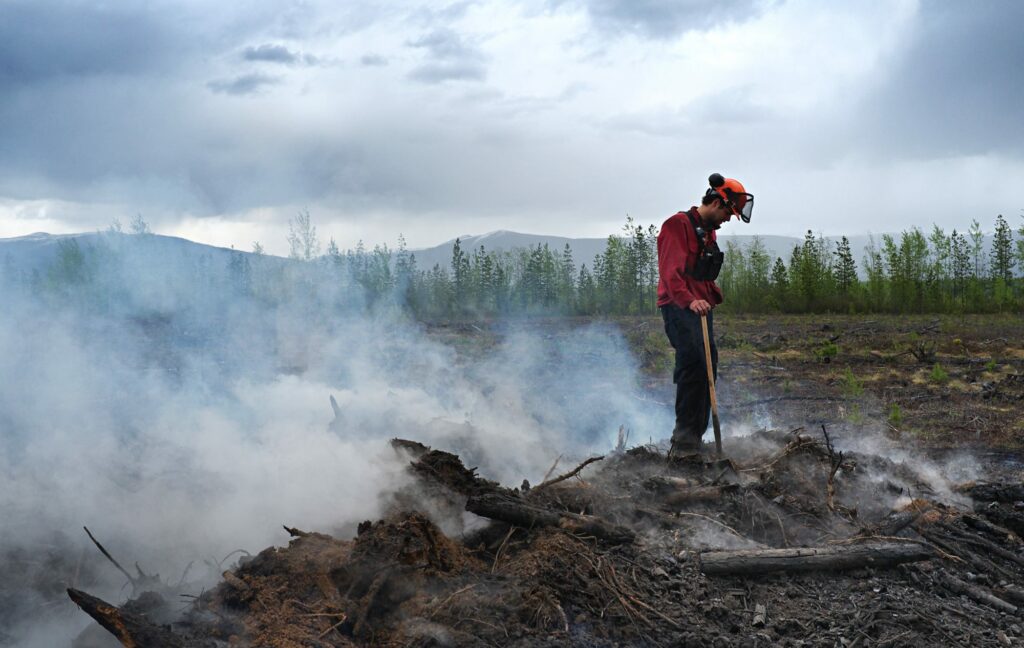 Firefighter standing on top of a smouldering pile of wood