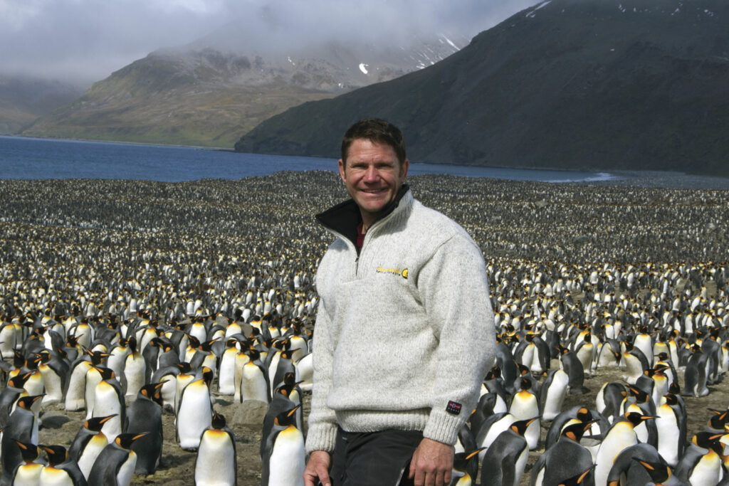 Steve Backshall stands on the shore among thousands of penguins