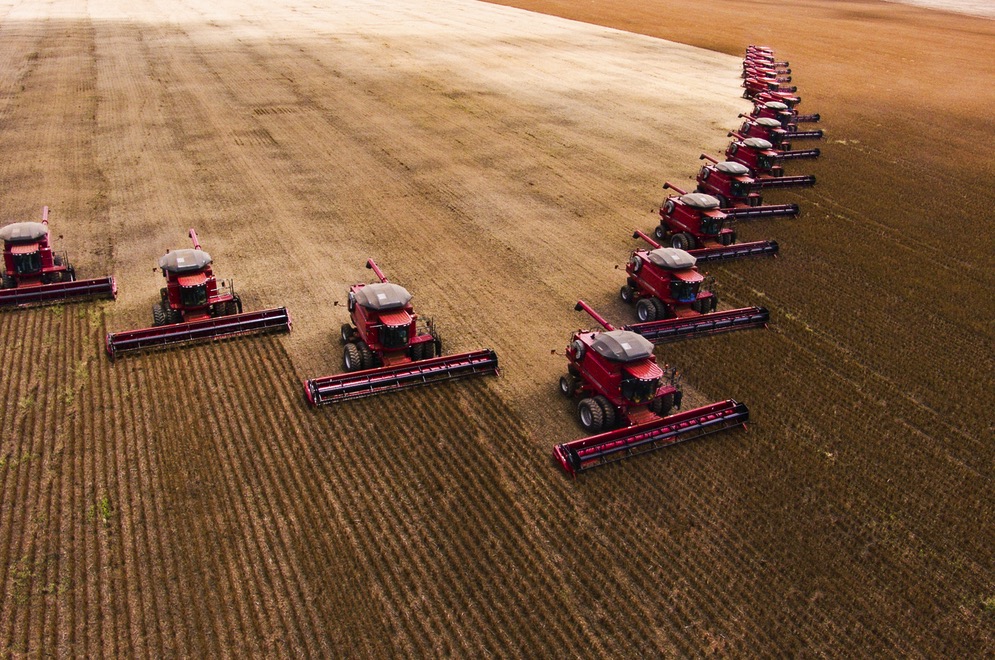 A row of combine harvesters collect grain in an enormous field