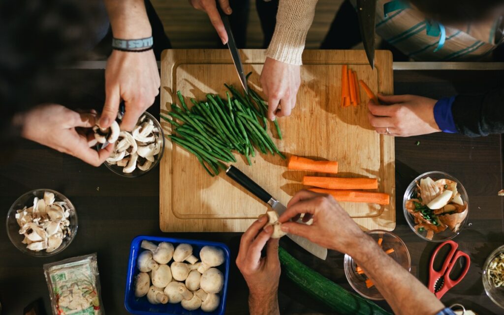 People gather round a chopping board to prepare carrots, green beans and mushrooms