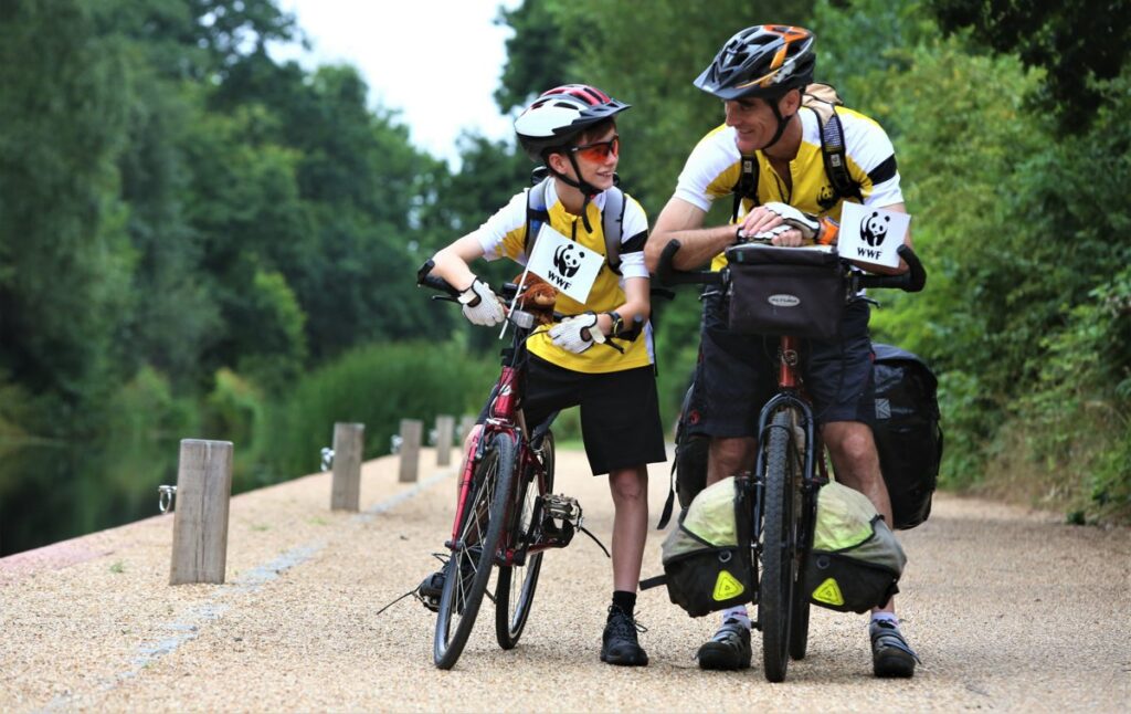 A father and son pose with their bikes, displaying WWF flags on their handlebars