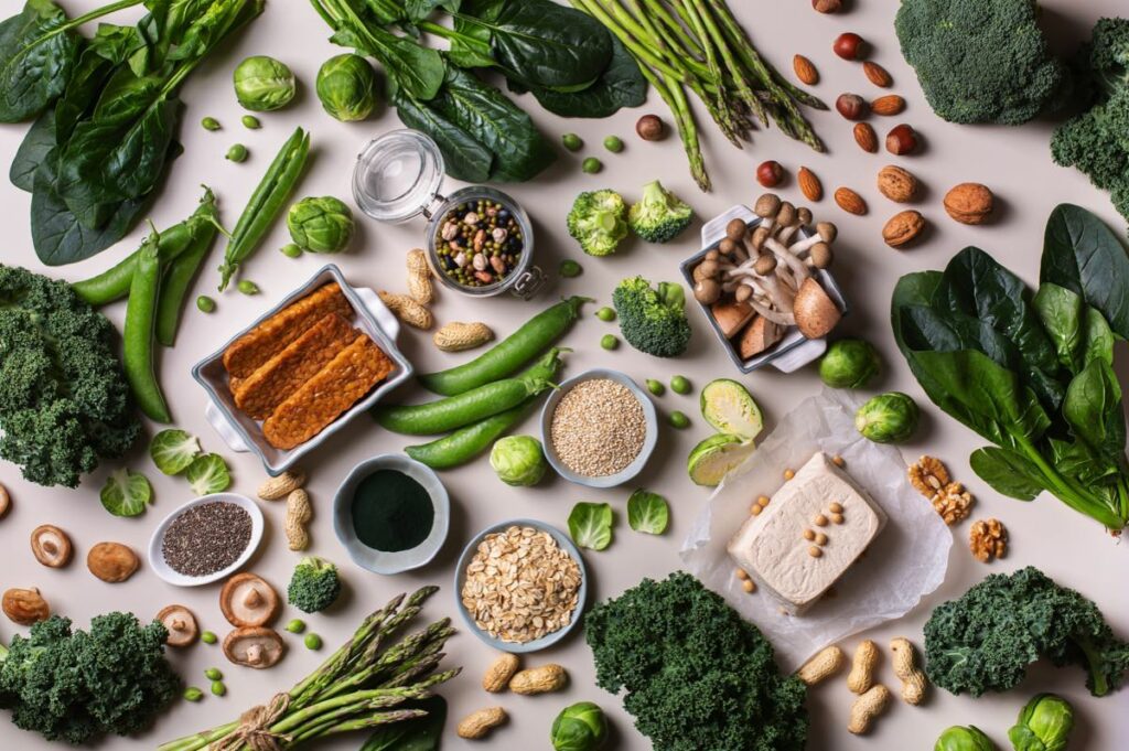 An overhead shot of a spread of nuts, seeds, leafy green vegetables and tofu