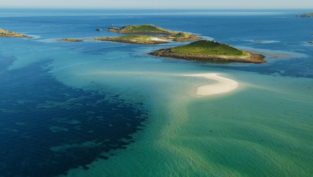 An aerial image shows a small group of islets off the UK coast, with green peaks and rocky shores, surrounded by turquoise sea