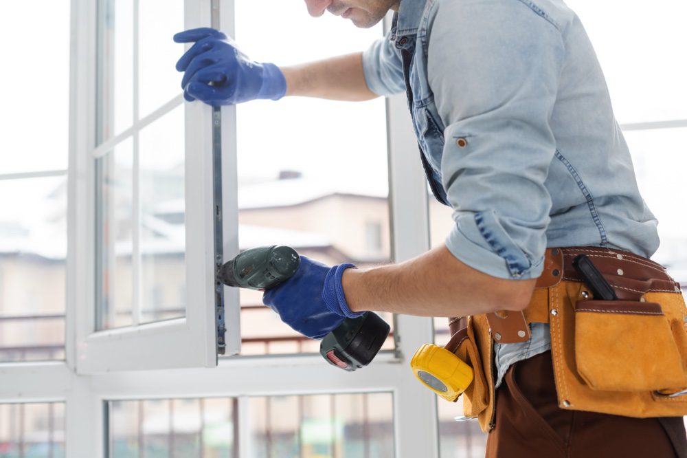 A workman wearing a utility belt installs new double-glazed windows