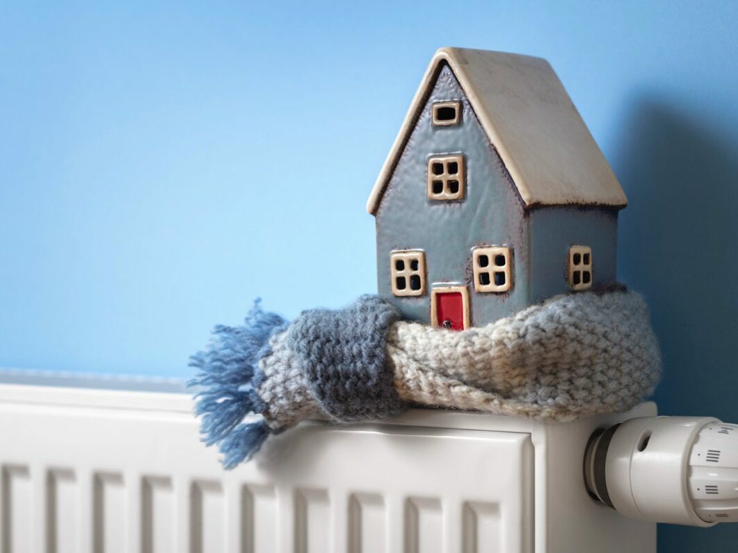 A model of a house sits wrapped in scarf on domestic radiator