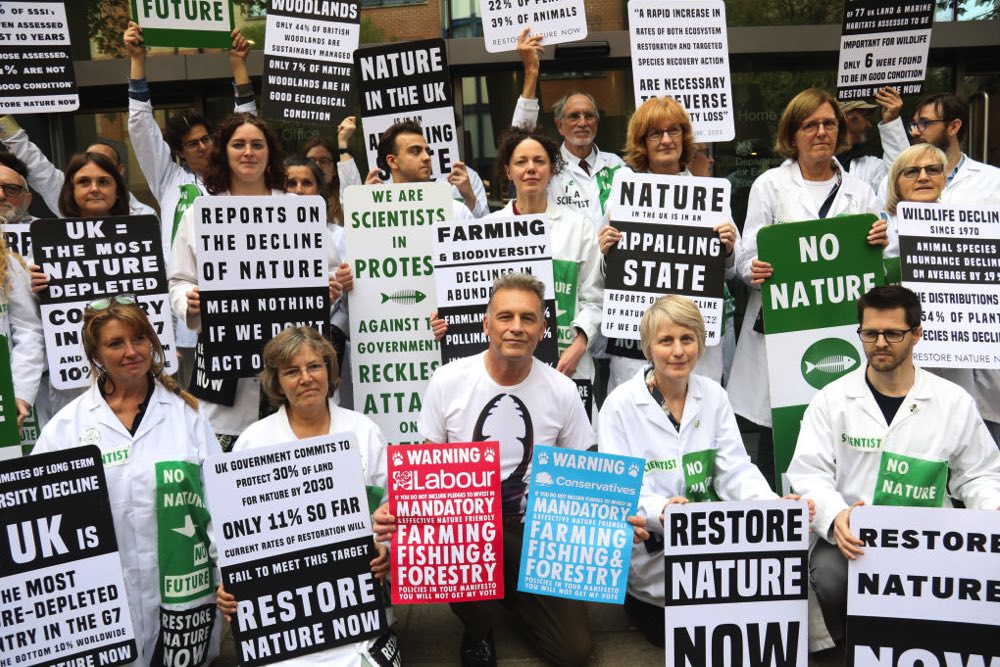 Naturalist Chris Packham poses with a large group of scientists, all holding placards at the Restore Nature Now demonstration