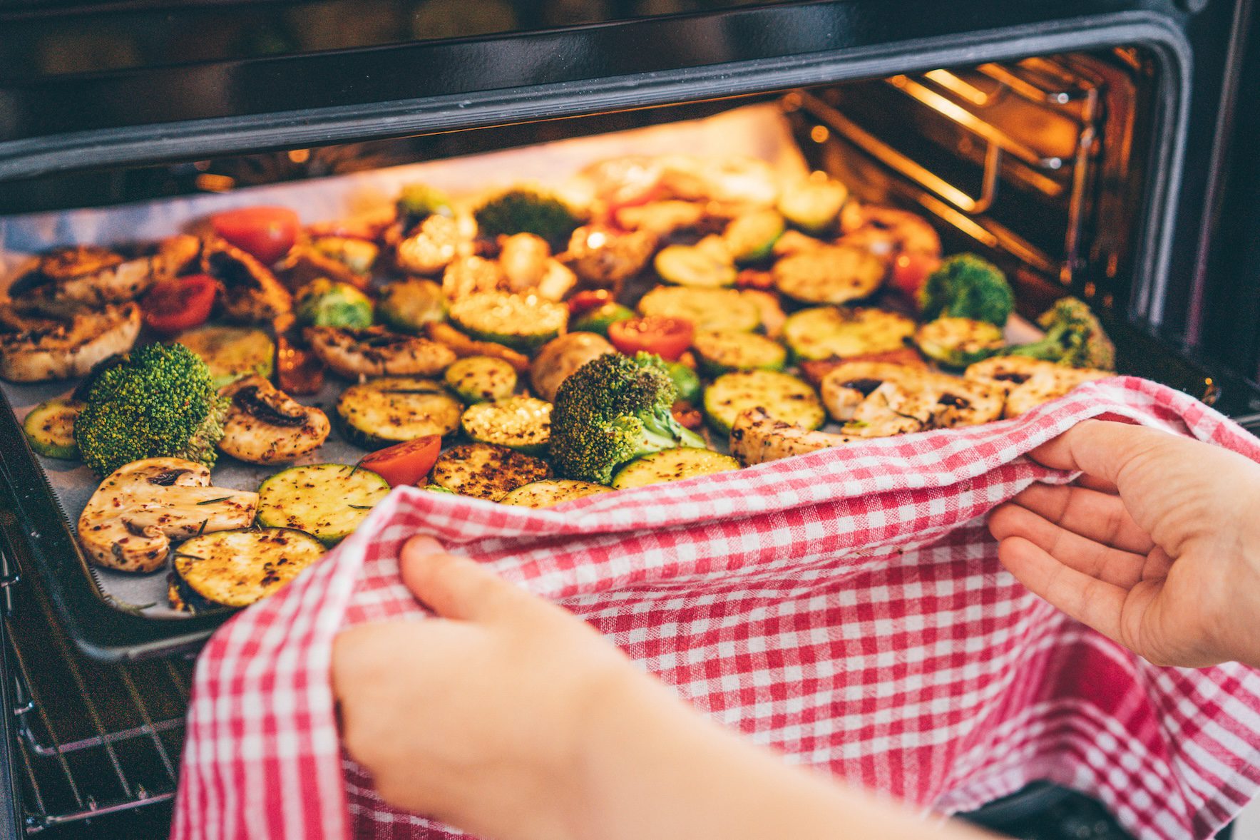 A close up of someone putting a tray of vegetables in an oven.