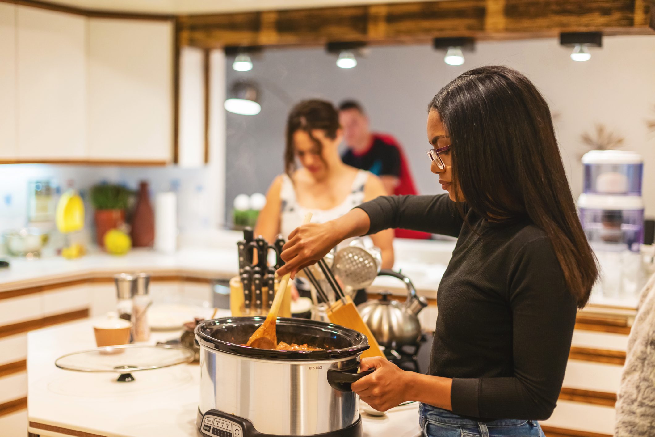 A group of young people in a kitchen, with someone serving a meal from a slow cooker