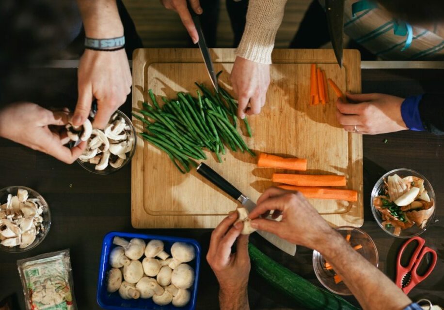 People gather round a chopping board to prepare carrots, green beans and mushrooms