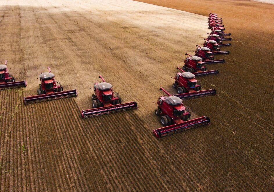 A row of combine harvesters collect grain in an enormous field